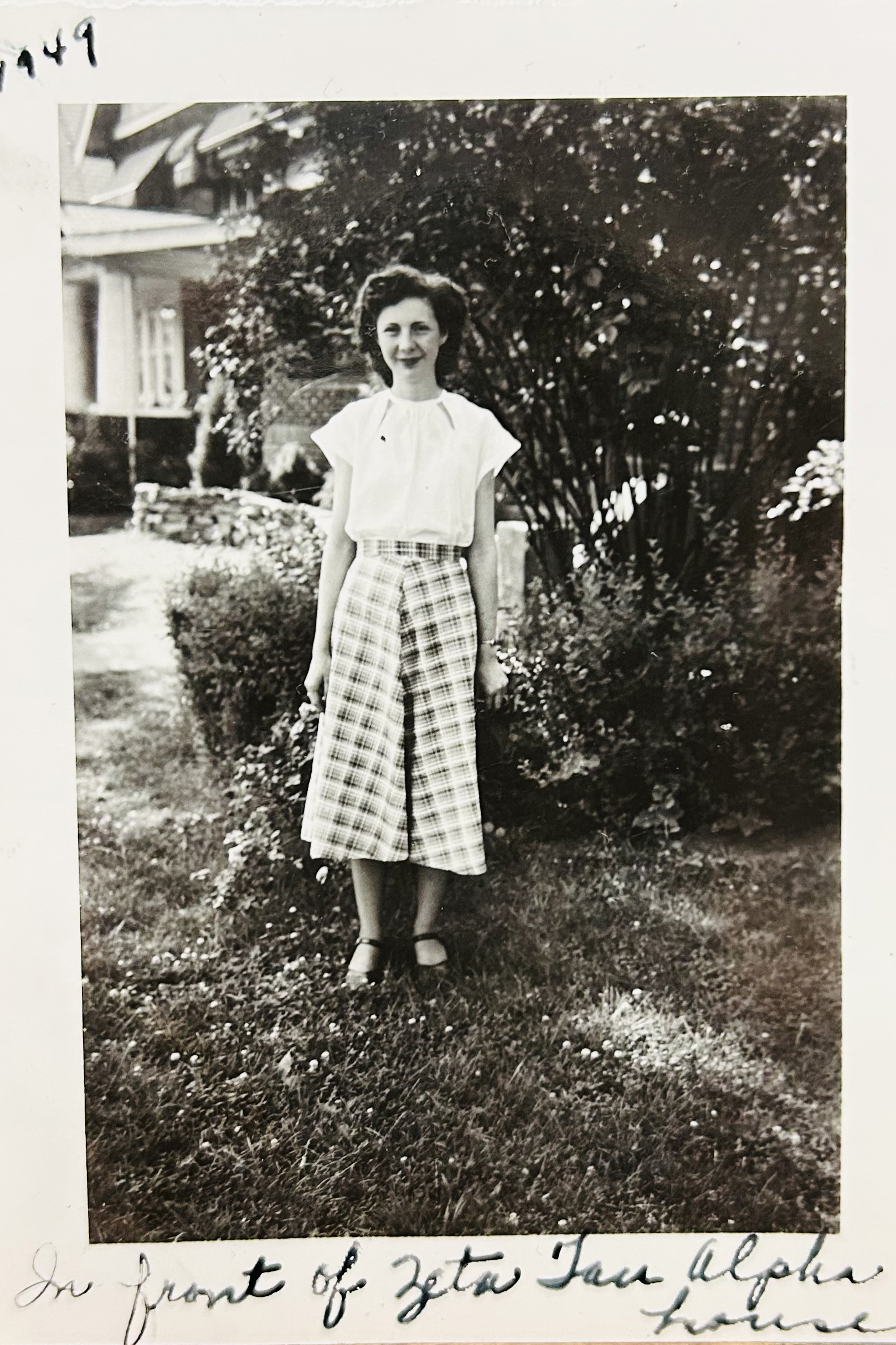 As a young woman in this black and white photo, Ruth Klingler McPheron stands in front of a house and greenery wearing a white blouse and shin-length plaid skirt. She is a white woman with a pretty hairstyle, a soft smile and the looks of someone you'd want to tell stories to.