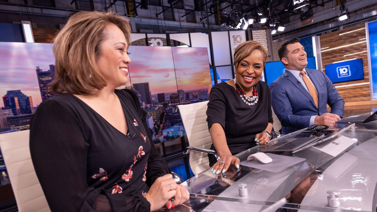 Tracy Townsend is seriously laughing as she puts her hand down on the long studio desk. She’s looking toward colleague Angela An, who is smiling. On Tracy’s other side sits Clay Gordon. He is also laughing. The three, who are on air, are all dressed up and seem well in-tune in their amusement