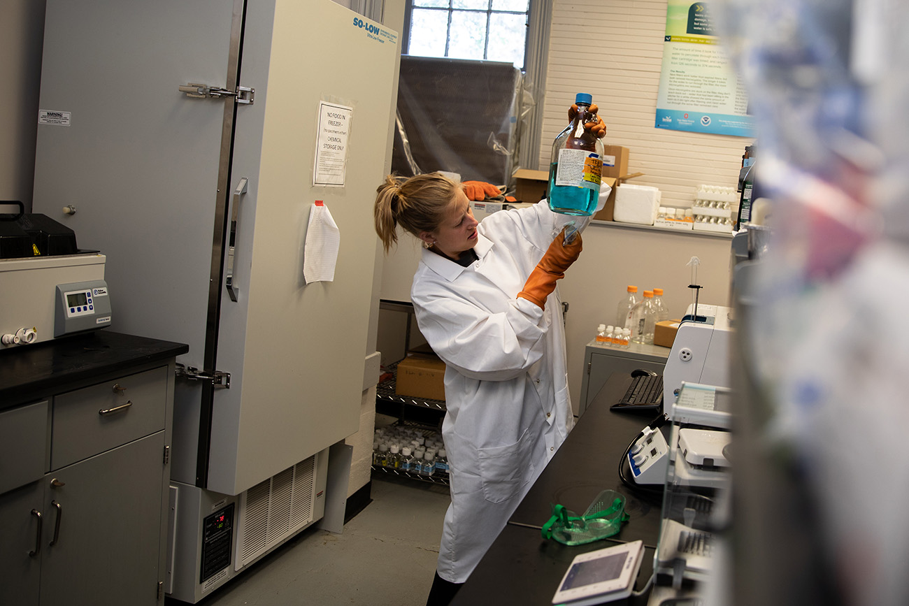 A college student with her hair in a ponytail performs water testing in a laboratory.
