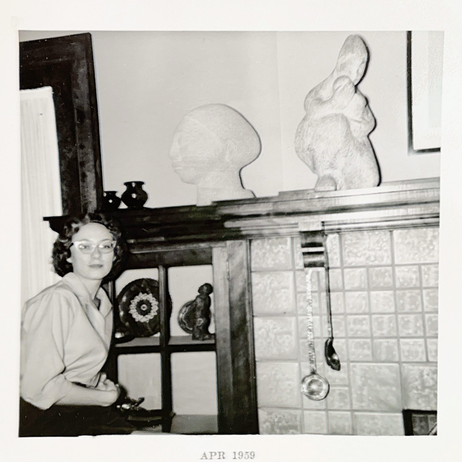 A younger Zehr sits in a living room near a fireplace and mantel. Surrounding it are large sculptures more abstract than realistic. She has on cats-eye glasses and looks quietly confident, just as she does in her more modern photo above.
