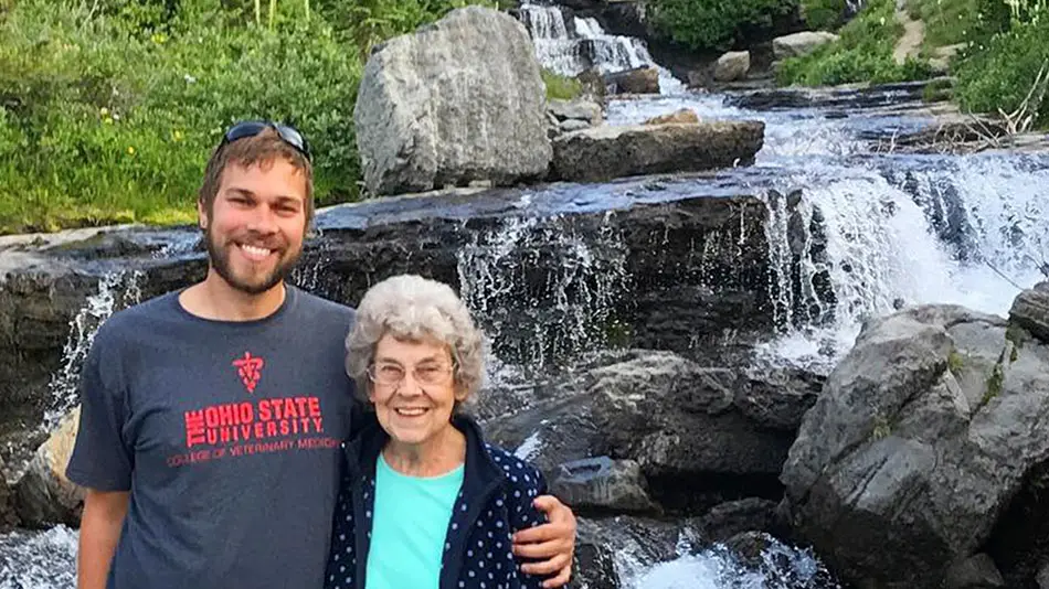 Brad is standing with his arm around Grandma Joy in front of a small waterfall. 