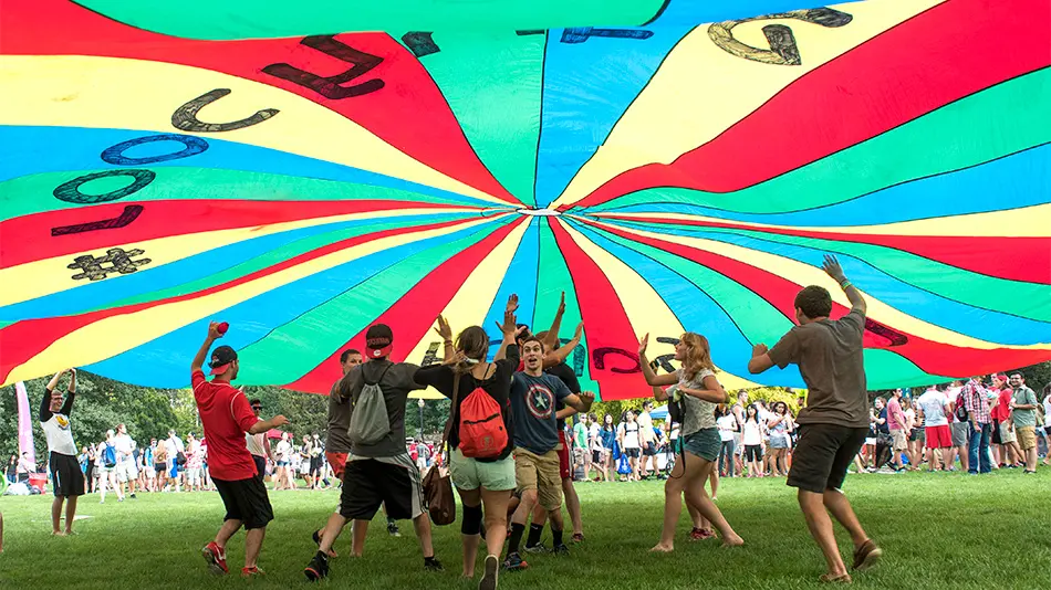 students playing under a bright colored parachute designed by Ron Holgado