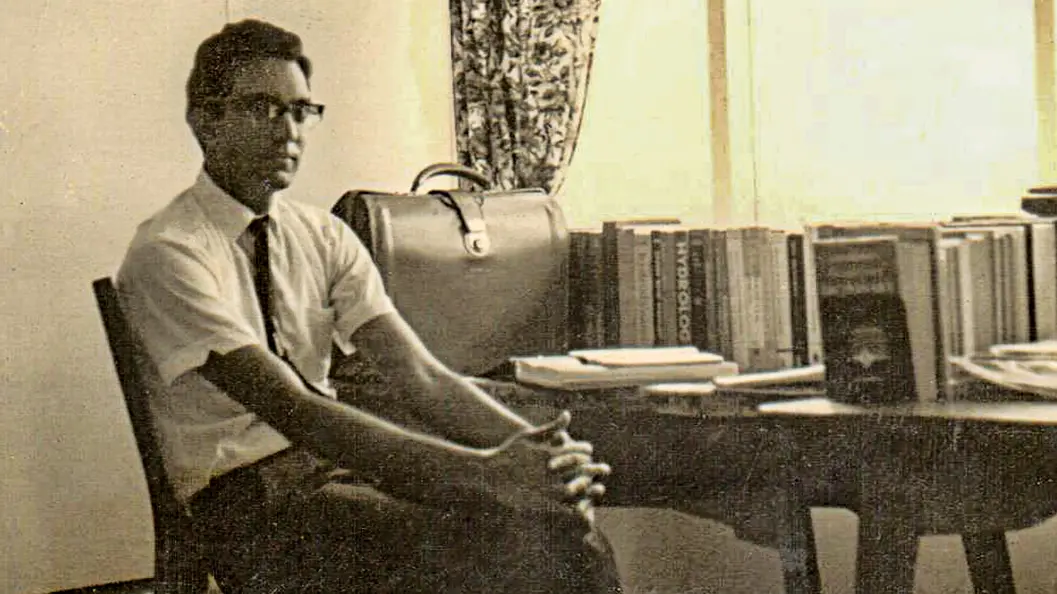 Sepia-toned photo of a young Rattan wearing a white shirt and tie and glasses.