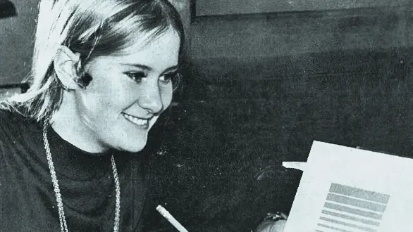 A black and white photo originally taken for a story in The Lantern student newspaper shows a college student in the 1960s looking at a square paper she’s holding with an emblem she designed for the Byrd Polar and Climate Research Center. The logo is a rectangle of bars of different thicknesses separated by different widths of negative space.
