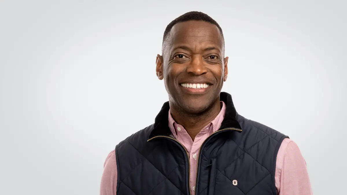 A black man with short hair, a wide smile and very symmetrical facial features looks happy yet relaxed while posing for the photo