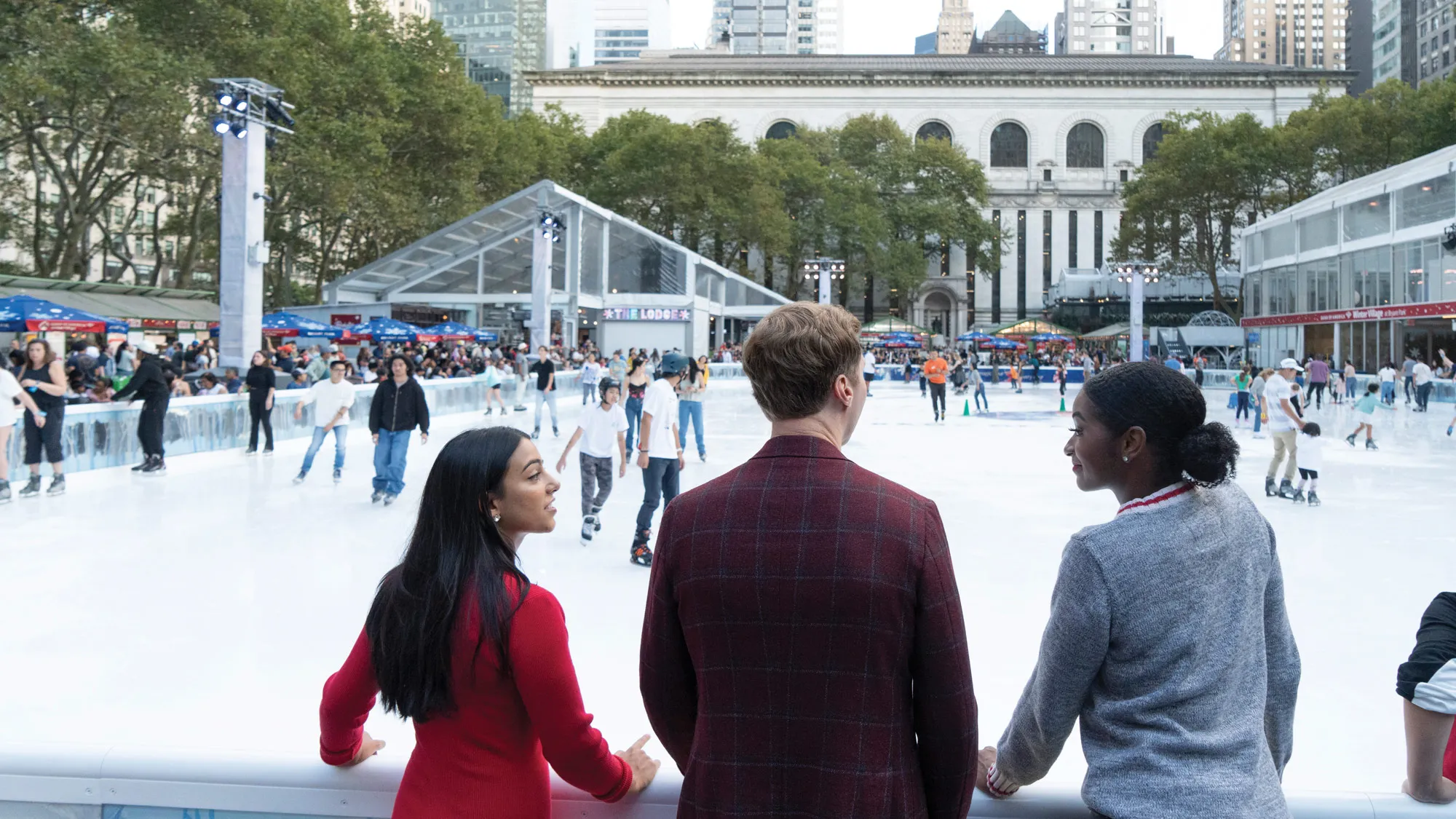 Three Buckeyes shown from behind watch ice skaters at a famous New York City outdoor rink.