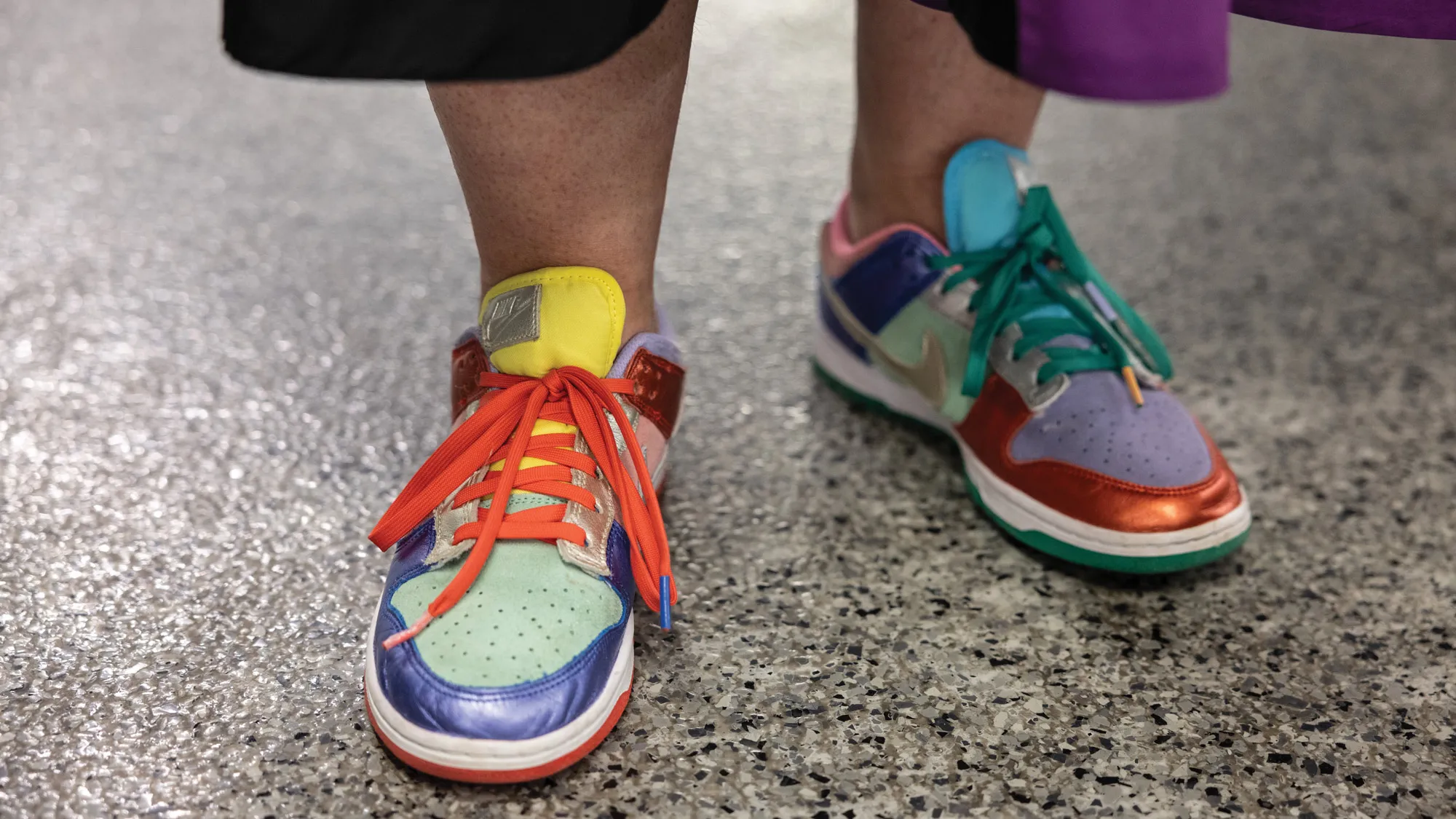 In a photo showing only Betsy’s feet, she wears a multicolored pair of unusual gym shoes, in that each shoe has color blocks in different positions. On one, the edge of the toe is shiny orange, the laces are teal and the rest of the front, purple. On the other, the edge of the toe is shiny blue, the laces are orange and the rest of the toe is teal.