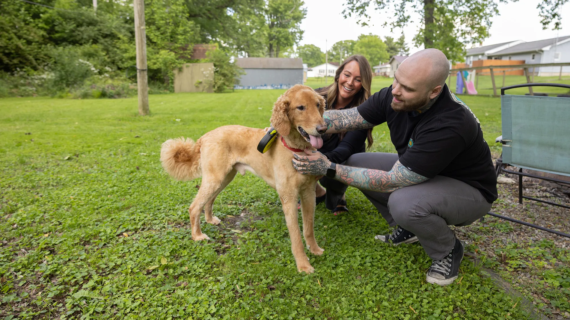 Zack and his sister, Kristine Jenkins, crouch in their backyard on a pretty day, petting a poodle looking dog that is the color or a golden retriever. The dog and the people seem happy.