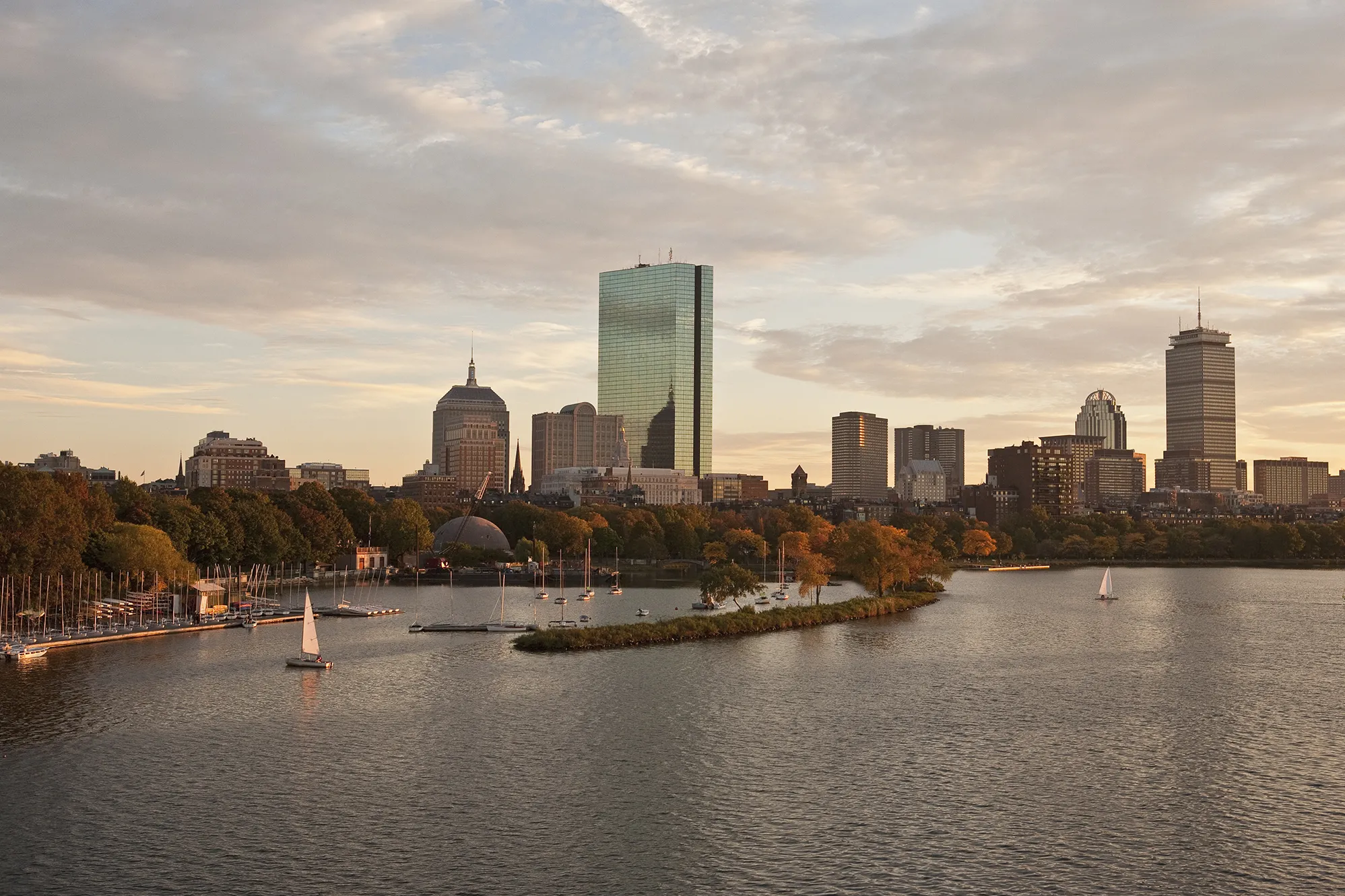 Boston’s skyline rises behind Boston Harbor at sunset.