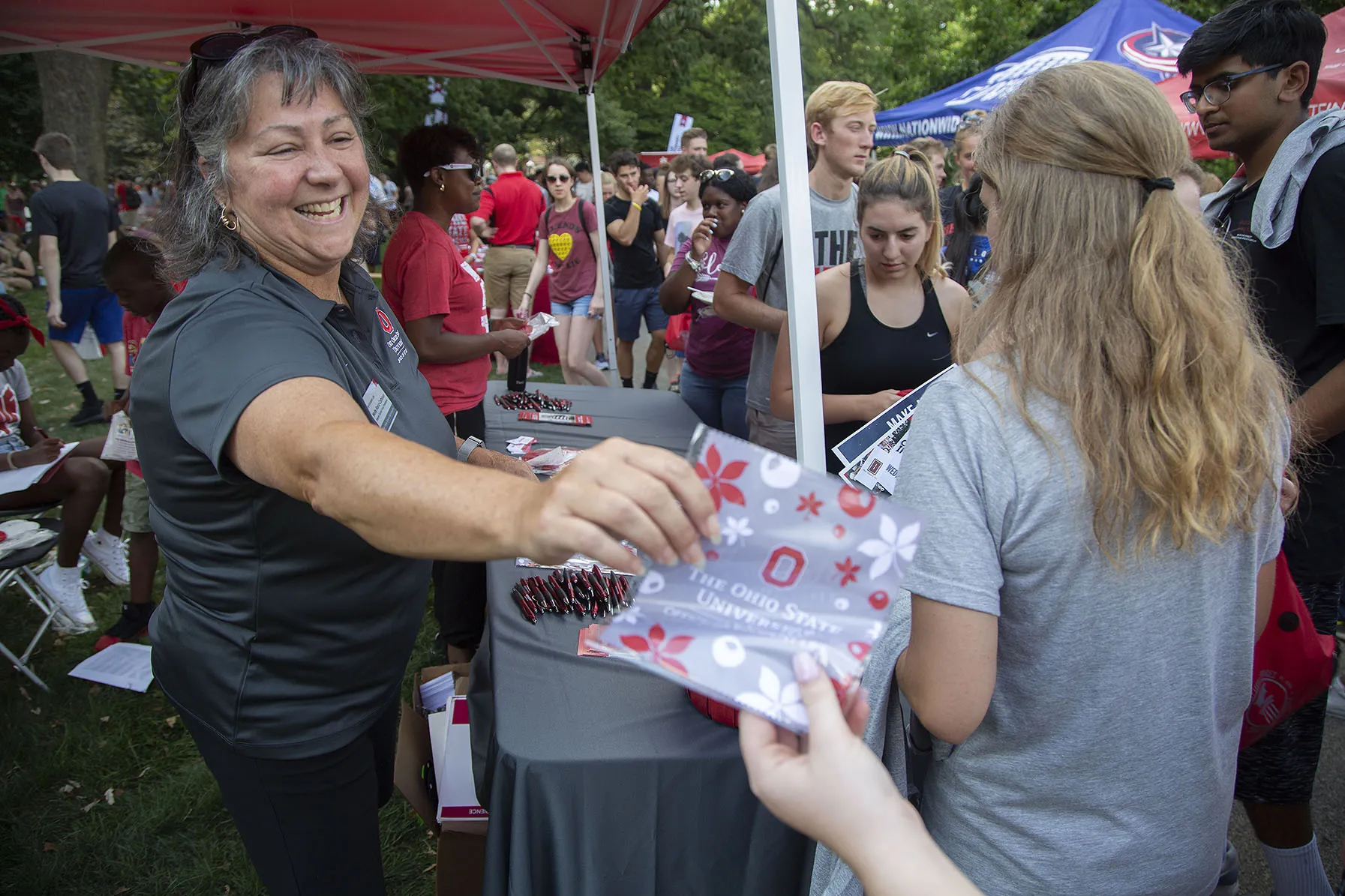 In a tented booth, Molly laughs as she passes out packets to students.