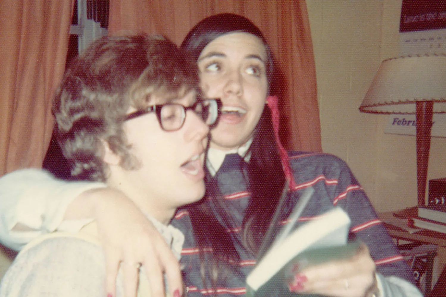 A couple seem to sing together in this photo from the 1970s. He wears glasses and she has long pigtails. Both are white.