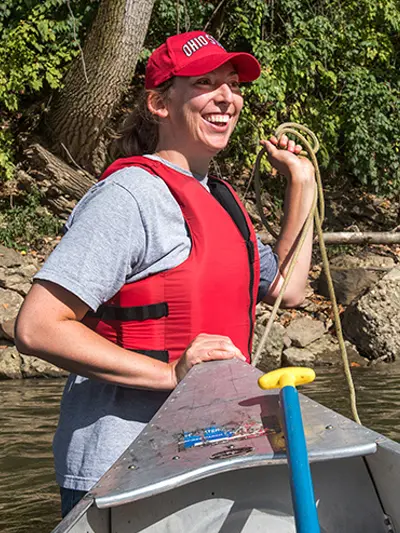 Monica DeMeglio carrying a canoe with a life vest on