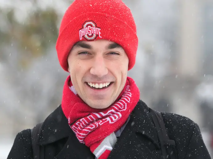 Person in red ohio state winter hat and scarf smiling in the snow