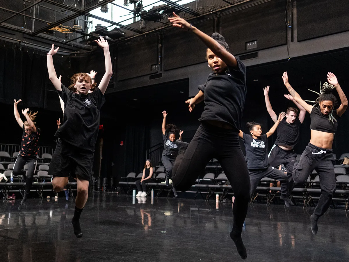 Seven dancers wearing black clothes—the color being the clothes’ only similarity—leap into the air with arms extended above their heads as they enact a scene from the island in “The Tempest.”