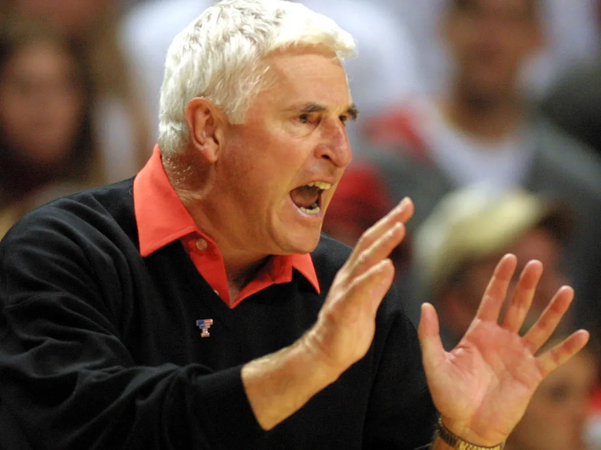 Coach Bobby Knight gestures with both hands as he yells at his team on the court. He looks focused and intense.