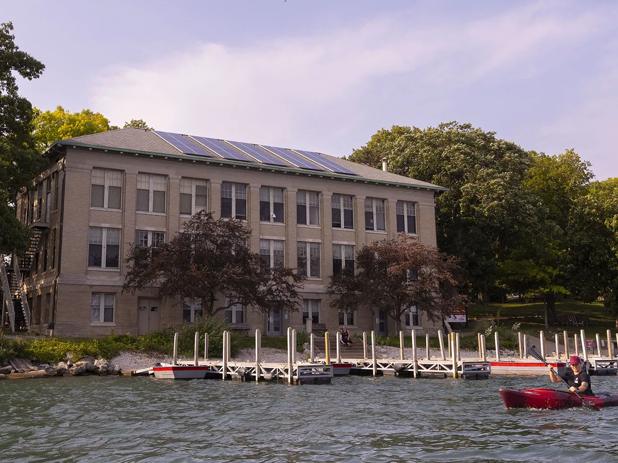A kayaker in Lake Erie paddles past a three story, rectangular building constructed of a light-colored stone