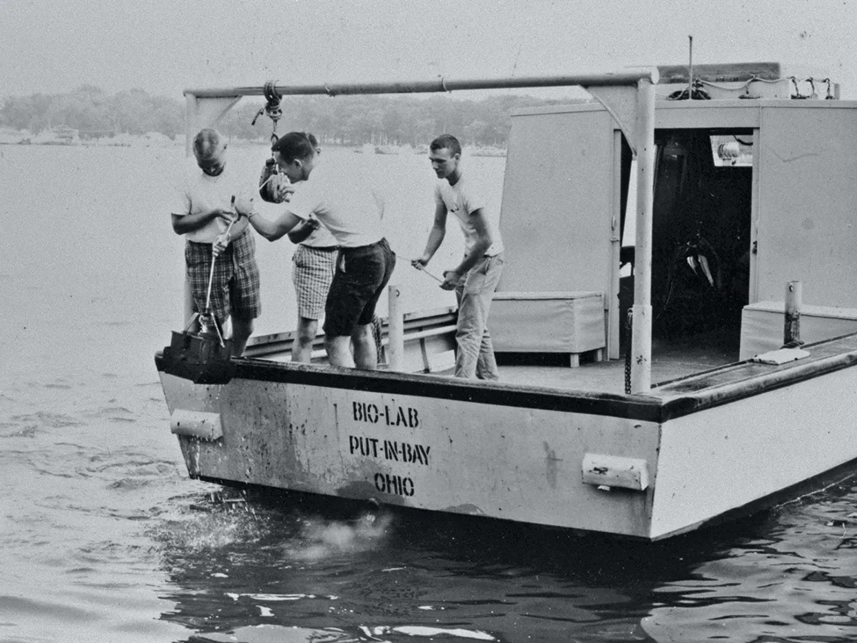 Young men on an old-fashioned boat wear shorts and work together to pull up a tow line