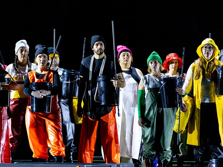 Actors in colorful costumes stand in front of a black background. They are loosely styled after fishermen, but in a way that's far more fun.