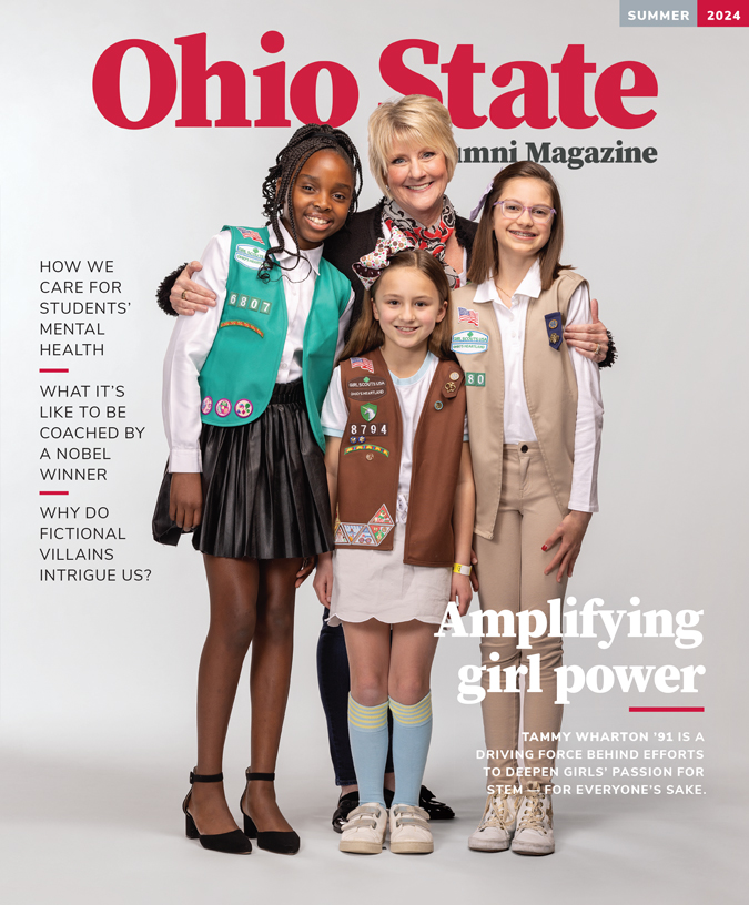 On the cover of the summer 2024 edition of Ohio State Alumni Magazine, Tammy Wharton, a white woman with short blond hair and a friendly smile, looks directly at the viewer while she has her arms wrapped around the Girl Scouts on either side of her. A third girl stands in front of her. The girls are all smiling, too, and dressed in their uniforms, they seem super pleased to be photographed with their leader.
