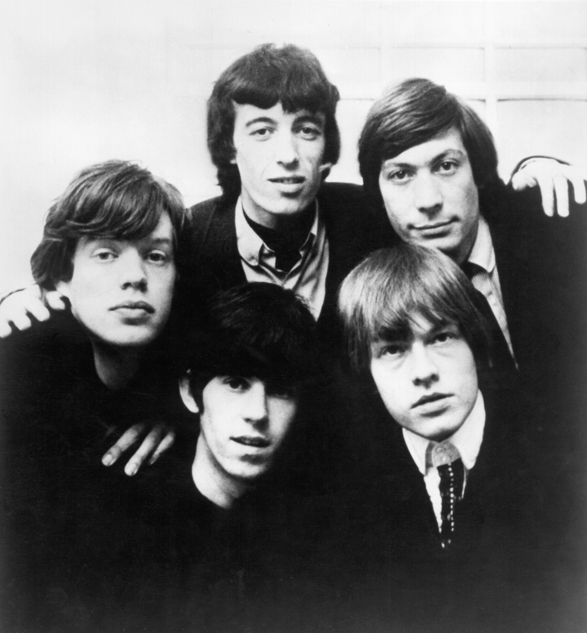 In a black and white photo, a group of young white man gather close for a portrait. They're only vaguely smiling.