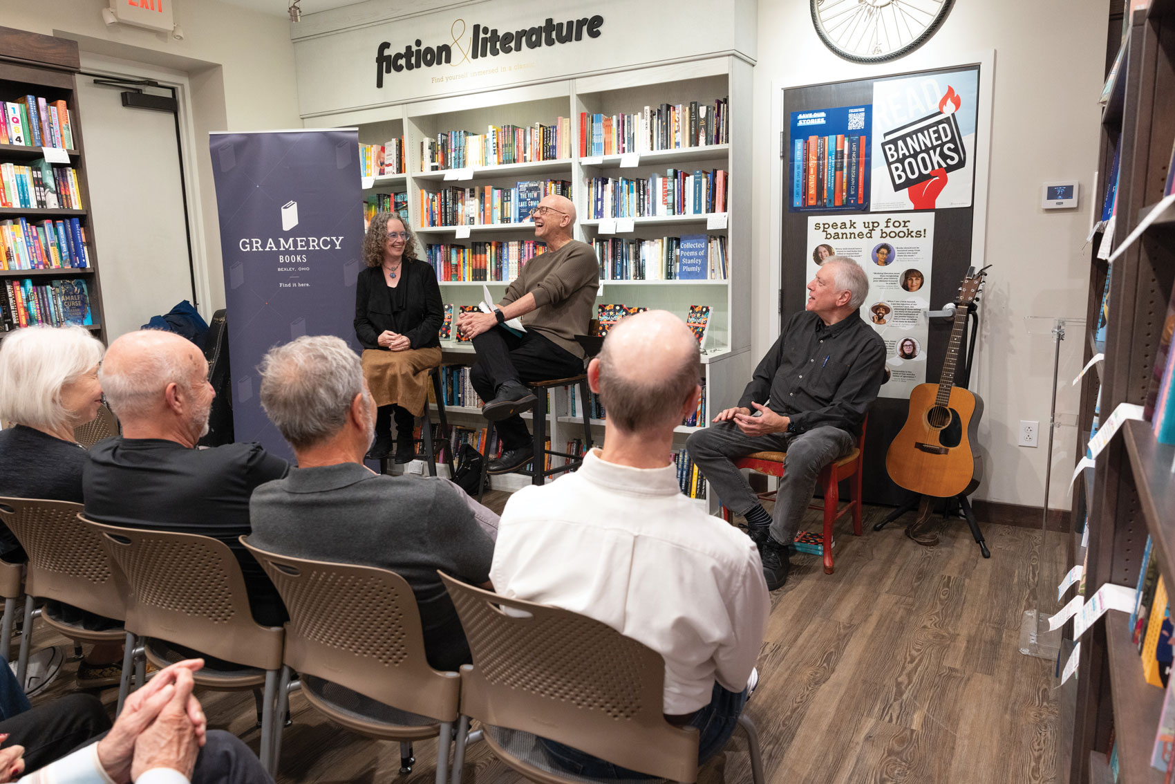 A woman and two men sit in front of the small crowd. They're laughing, and so are the people watching them.