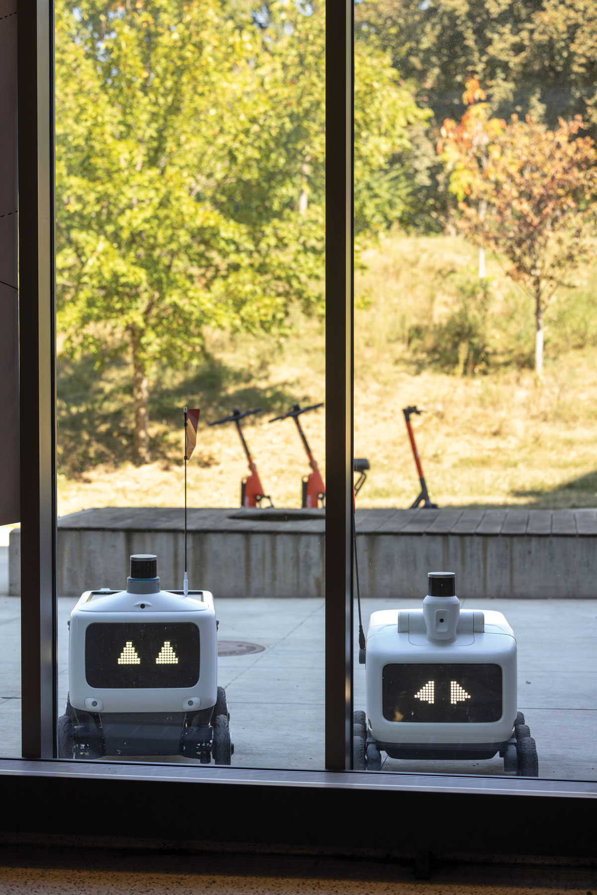 Two robots appear to look through windows into a building. In fact, they're waiting outside a restaurant for food to be added to them.