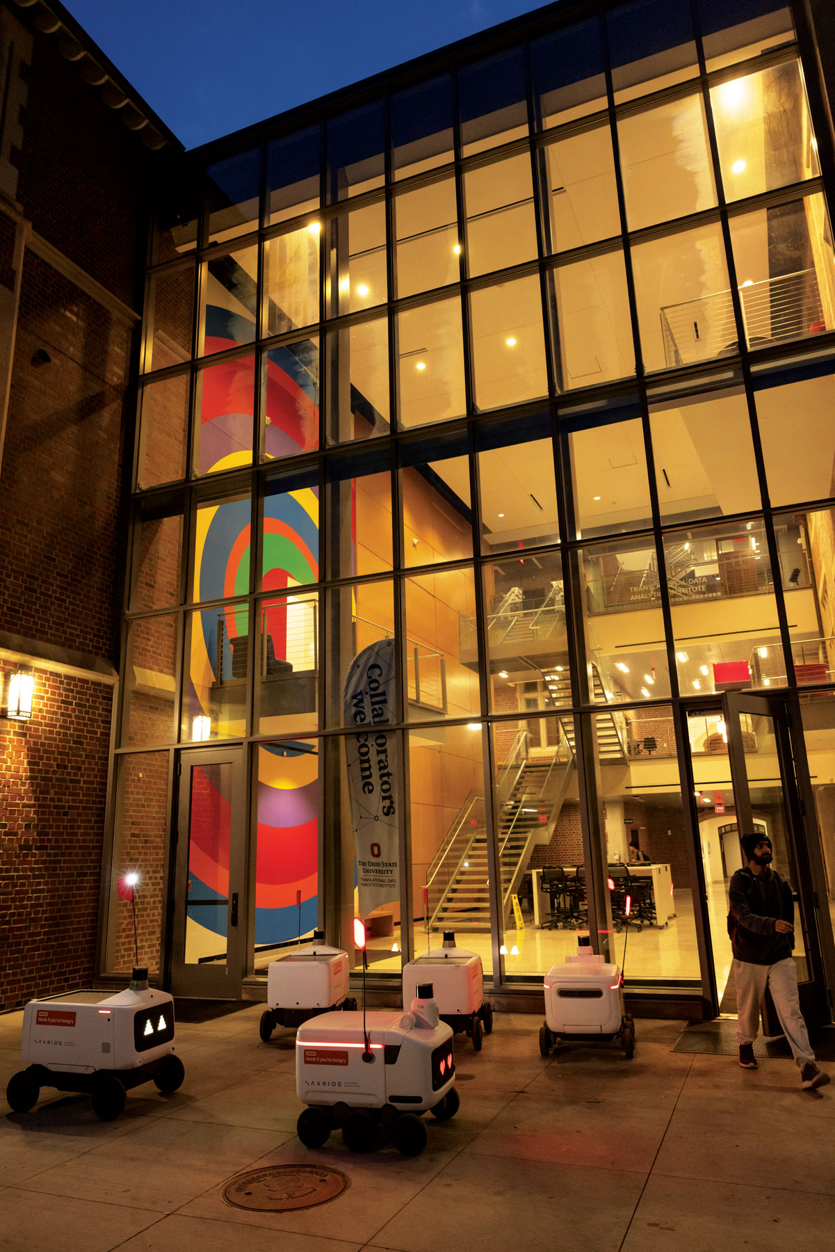 Pomerene Hall glows in the night as half a dozen robots gather outside to pick up food deliveries.