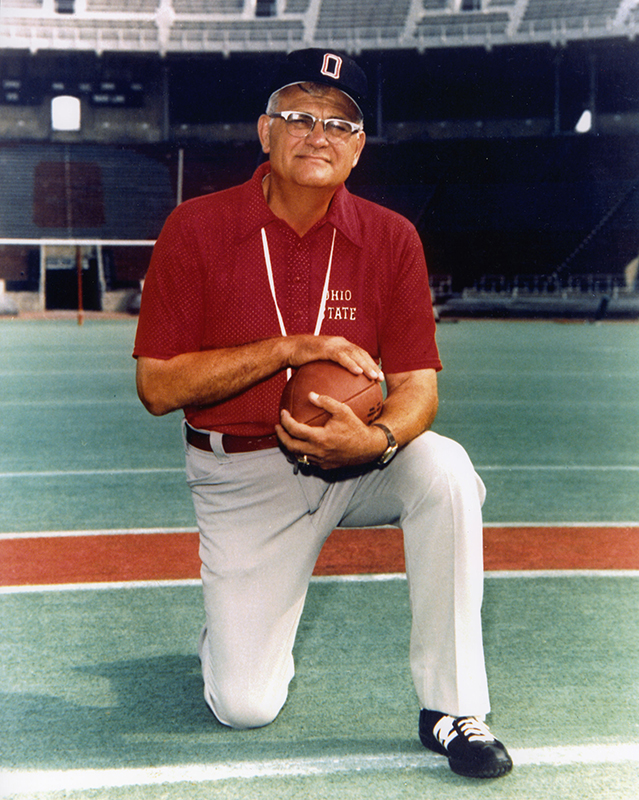 Woody Hayes kneels on the field while holding a football in 1978