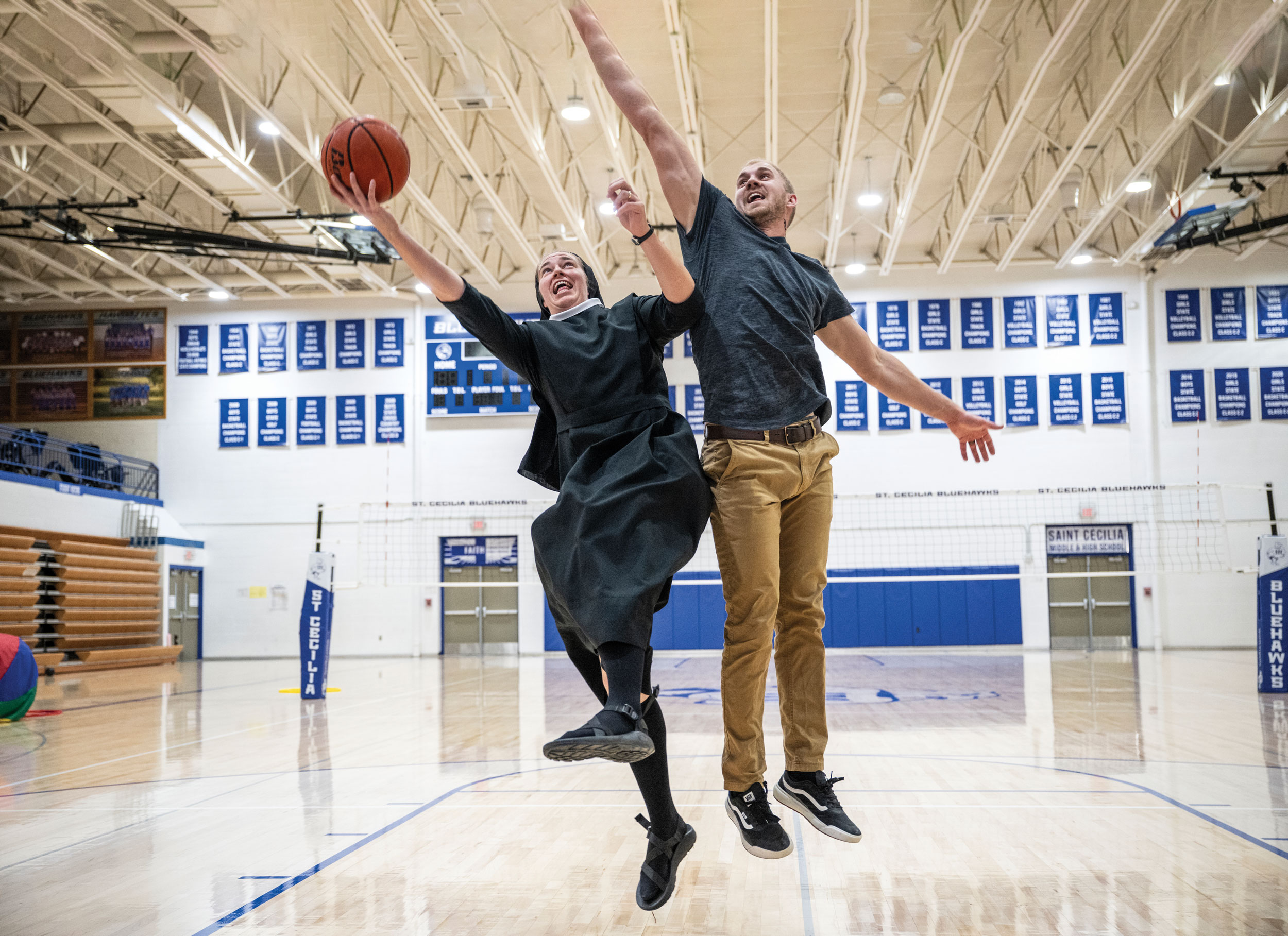 Sister jumps off the basketball court, dressed in her veil and habit, as he brother-in-law umps, too, trying to block her shot.