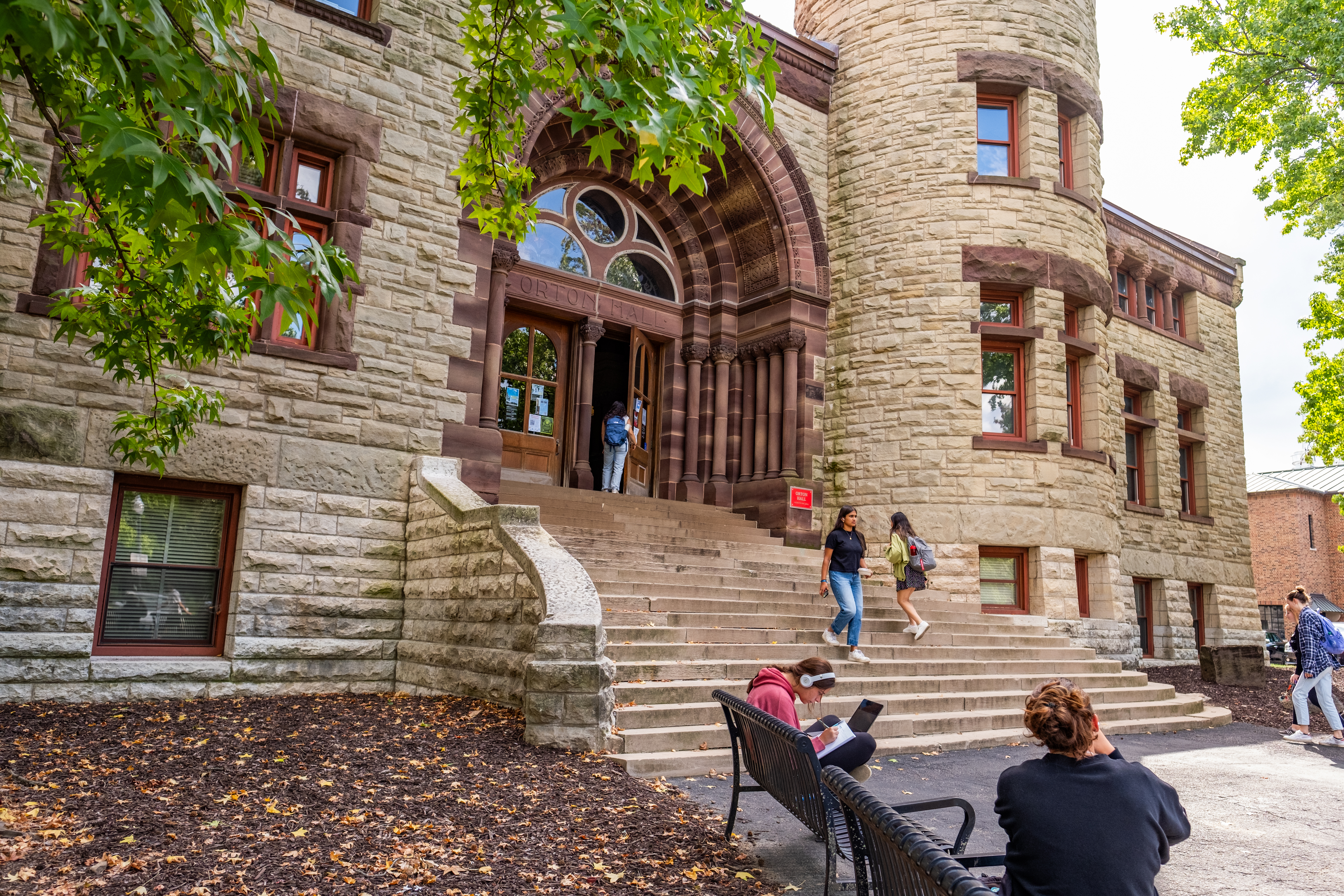 Orton hall is a stone building with 20 wide stone steps leading to the arched main entrance. The stone work is special and represents the different geological period of earth. Students walk in and out in this photo, which shows the stateliness of the building on a pretty day.