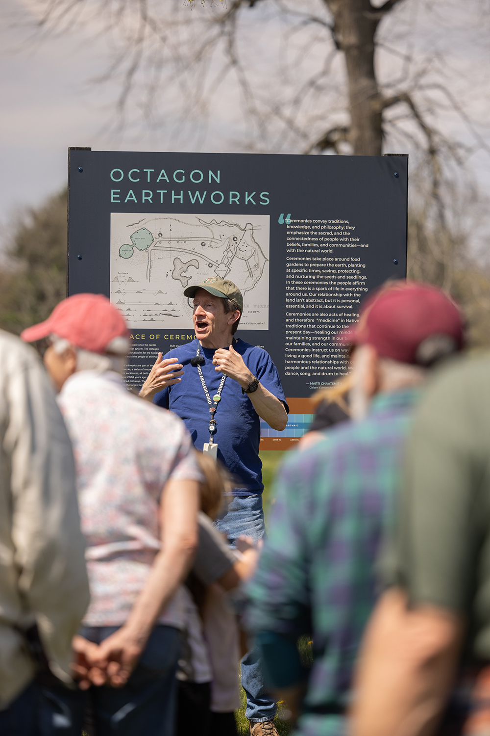Bradley Lepper explans a point about the Hopewell mounds to a small group. Behind him is a sign that says "Octagon Earthworks" and has a map.