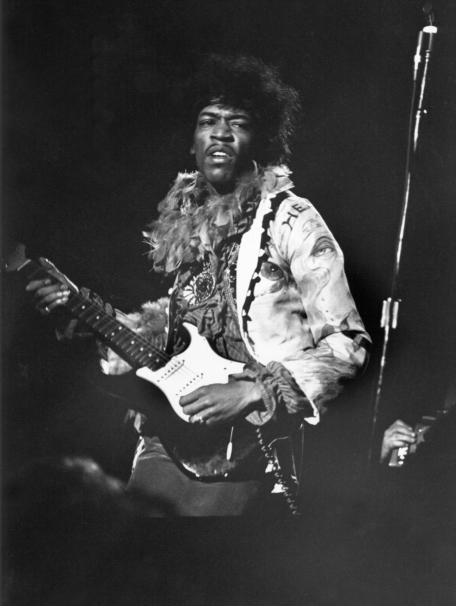 Jimi Hendrix, with his big hair and an expression that says he's feeling his music, plays his guitar on stage.