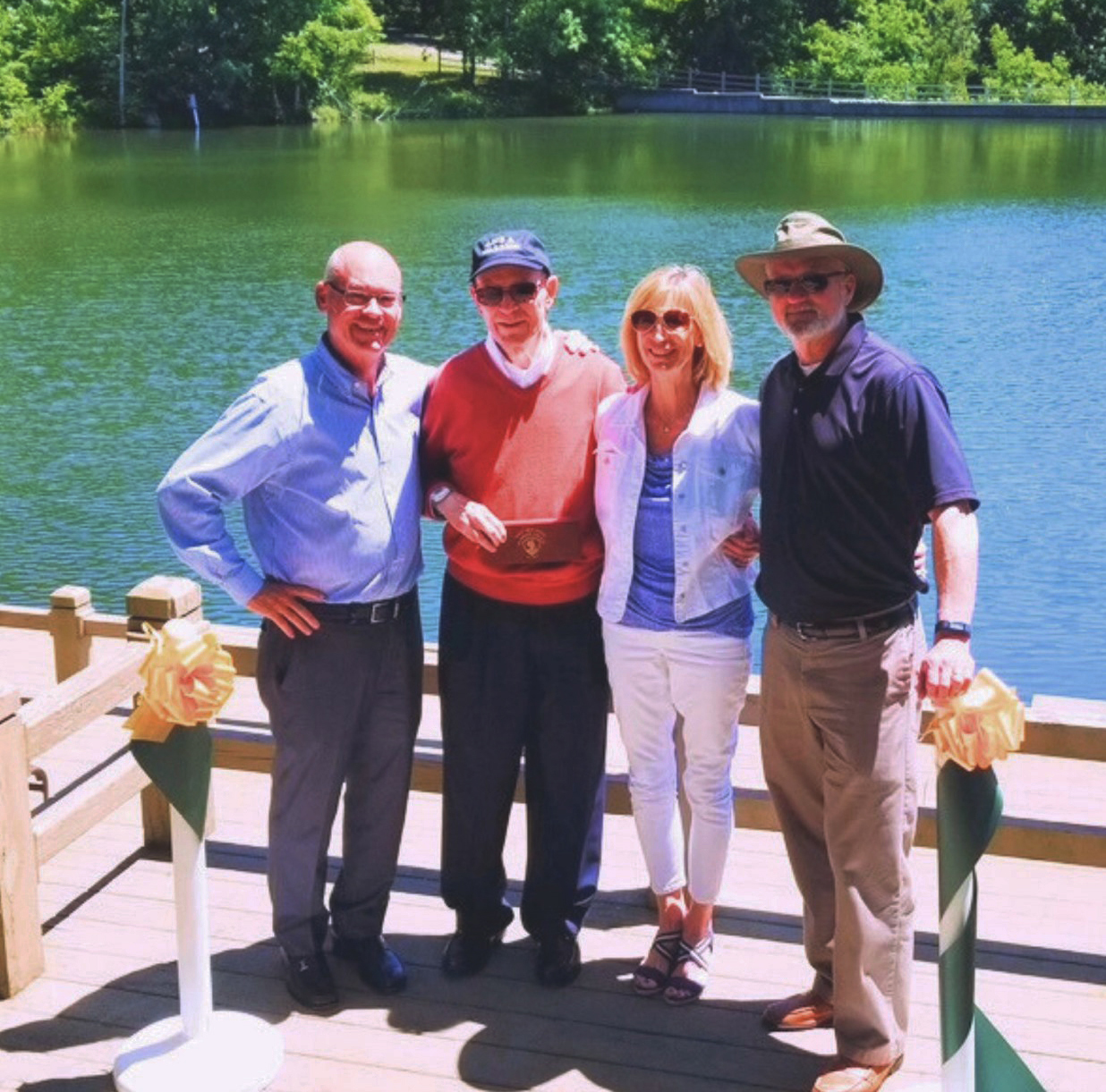 A family of four poses for a photo at the side of a lake.