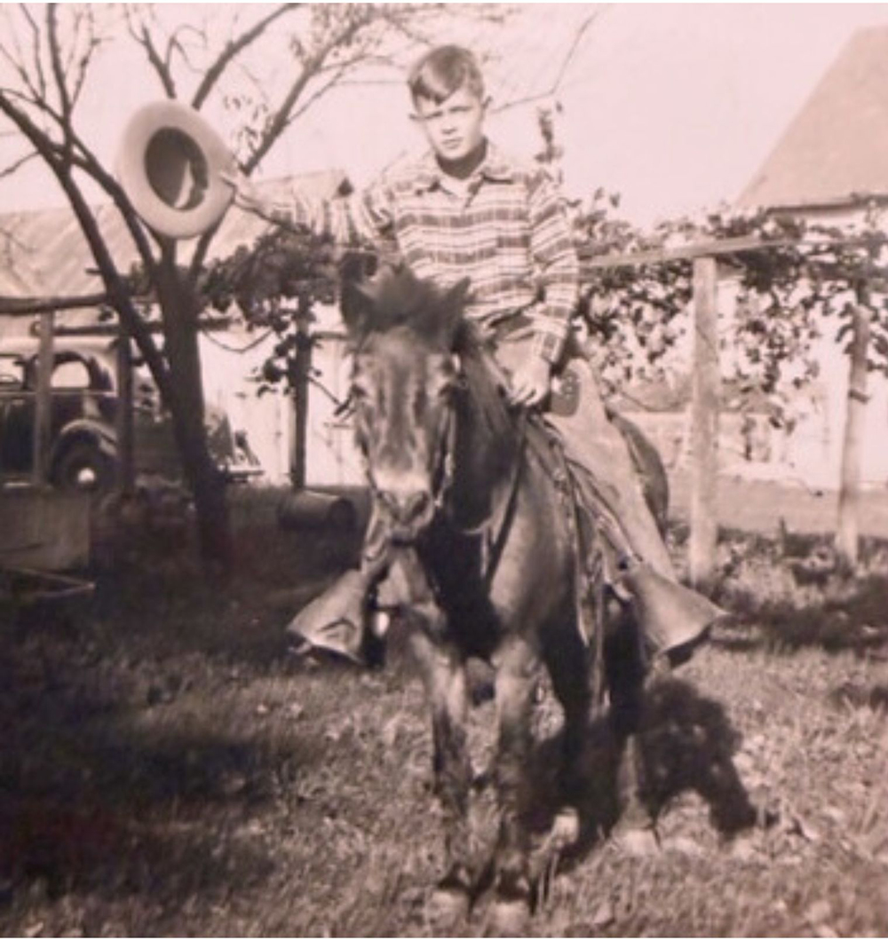 As a boy, Dick Wood sits on a pony. He's holding his cowboy hat off to the side with an outstretched arm, as if ready to take off for adventure.