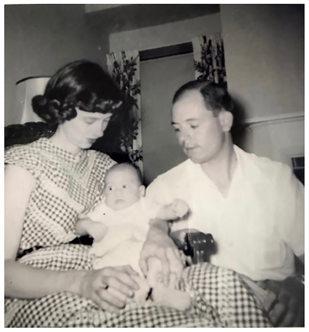 IN this old black and white photo, a woman and her hausband both watch a baby sitting on her lap.
