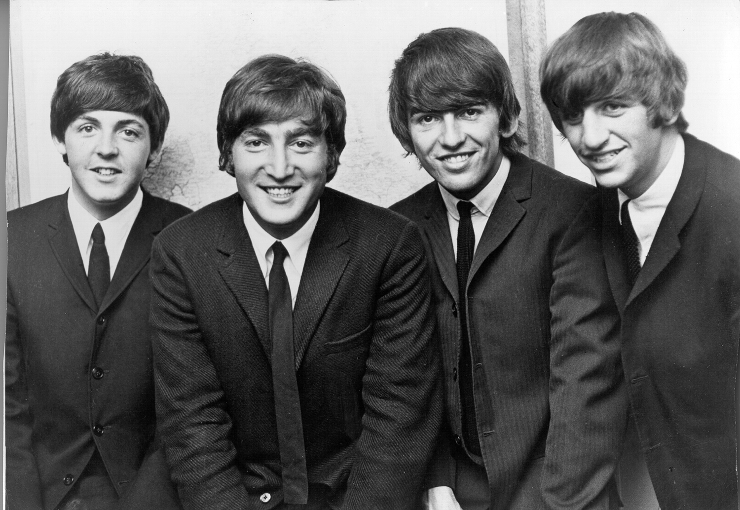 The Beatles pose for a photo. They all have big smiles and big hair.