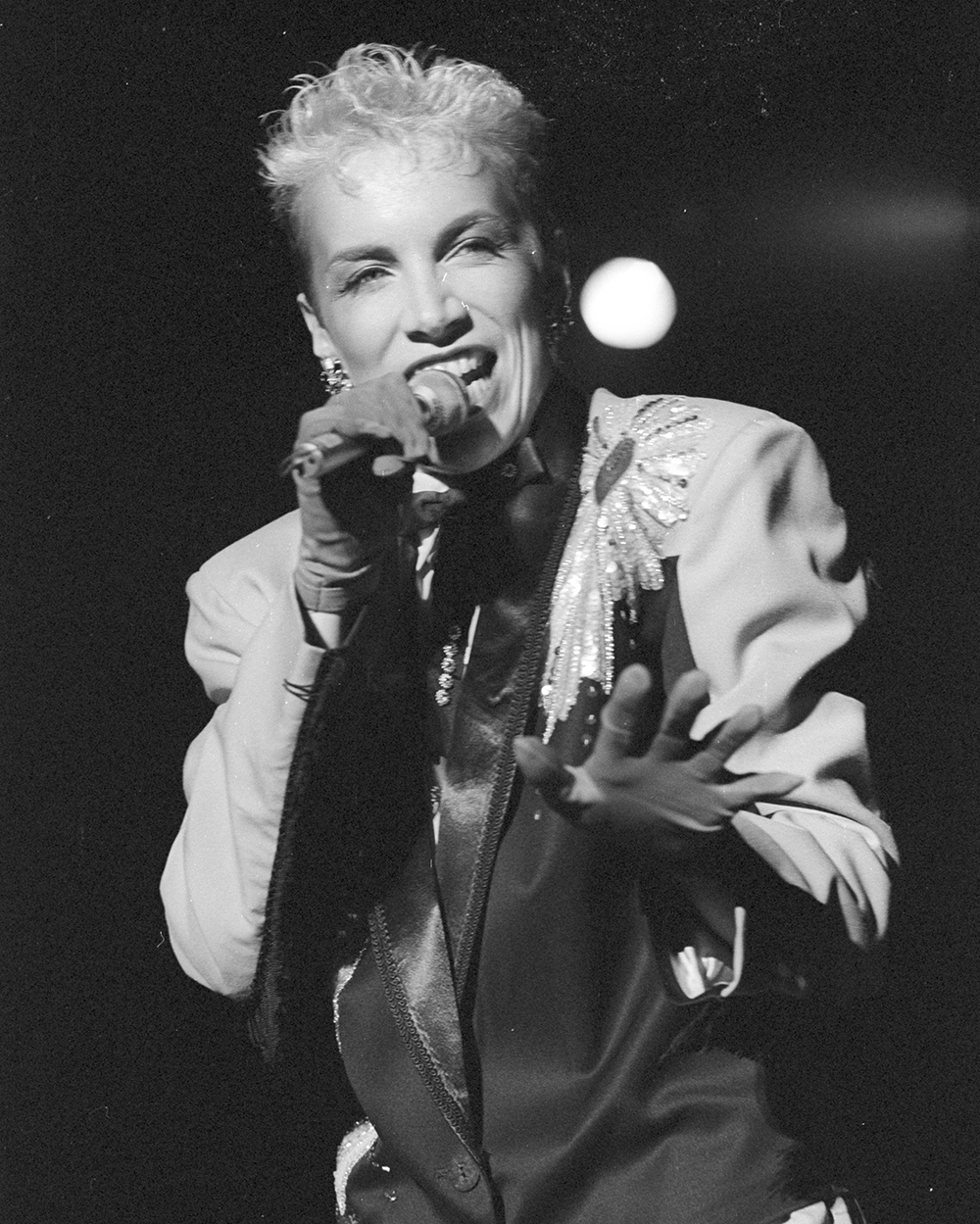 Annie Lennox, a white woman with short bleached hair, sings into a microphone on stage. She's beautiful despite not following the conventions of feminine beauty.