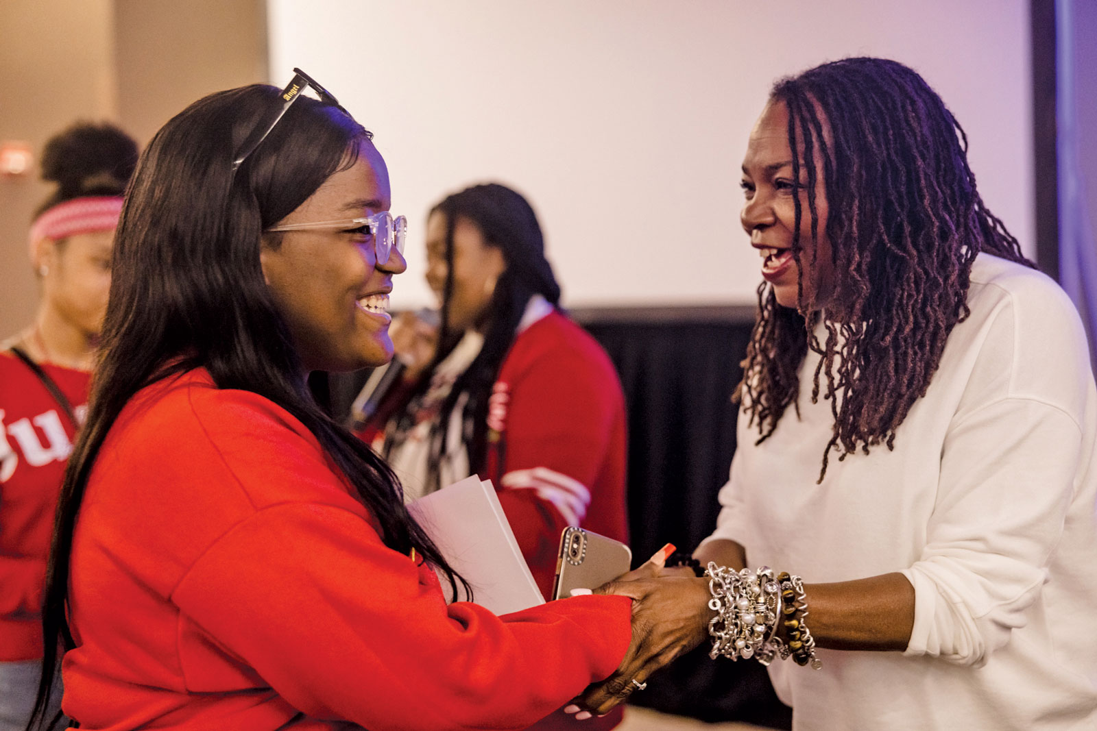 A woman greets a student. They're both smiling and clearly enjoying the interaction.