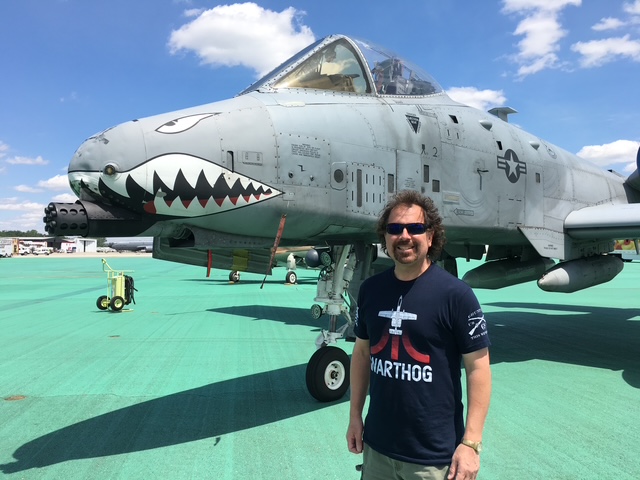 Richard HUghes poses for a photo in front of a historical airplane with a sharptoothed-grinning shark-like face painted on it.