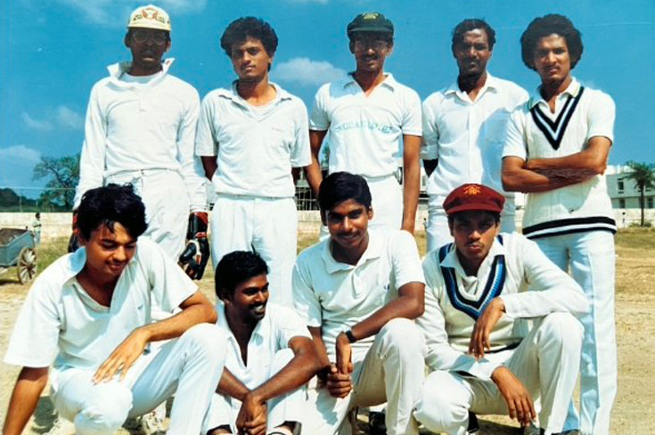 A cricket team poses for a photo. Each person wears white, and they're naturally posing. Some smile; some don't