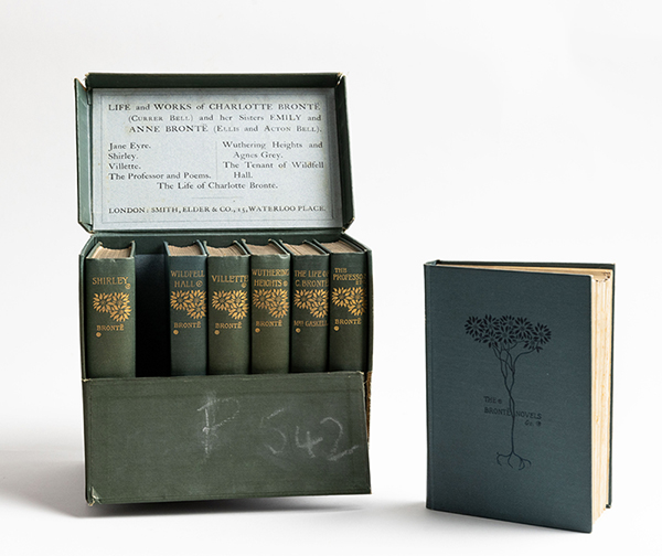 A dull green box, with P 542 lightly chalked on the front, has the hinged top open, showing 6 books of the same color and an empty space for one more. That book is sitting upright on its side, on the front is a simple drawing of flowers, their stems and roots. That book is titled “The Bronte Novels” and text inside the box’s open lid names the other books in the collection.