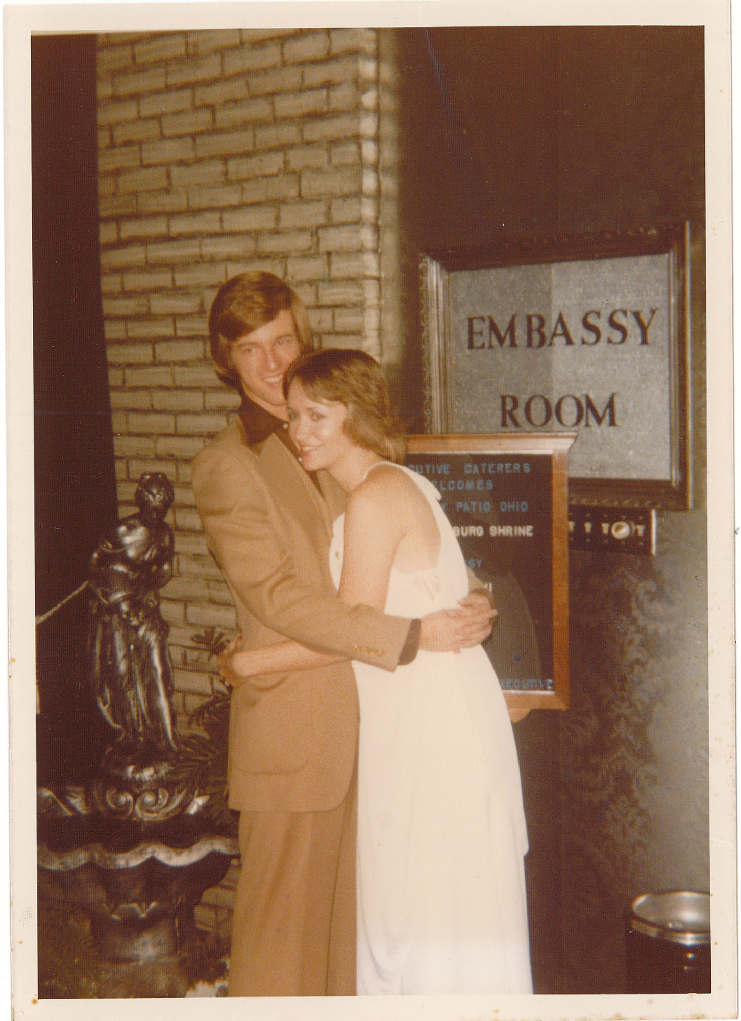 In this old photo, a college-age couple hugs as they pose, clearly comfortable being affectionate with each other. They’re both dressed up and have the feathery hair of the 1970s.