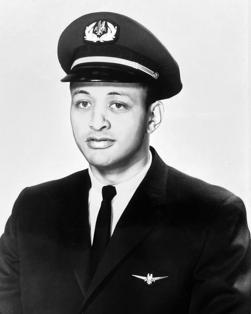 David Harris poses for an American Airlines headshot in a suit and narrow tie and pilot’s hat. He is a Black man and his expression says he is serious yet open or trustworthy—like someone you’d trust to fly your plane.