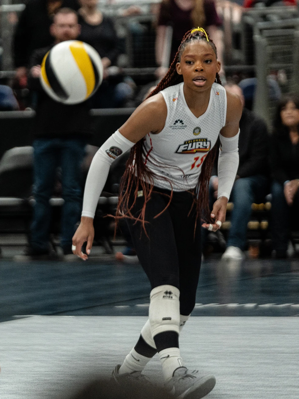 Jenaisya Moore focuses on the volleyball during a match. Fans line the stands behind the young Black woman, who has braided hair so long, it passes her waist.