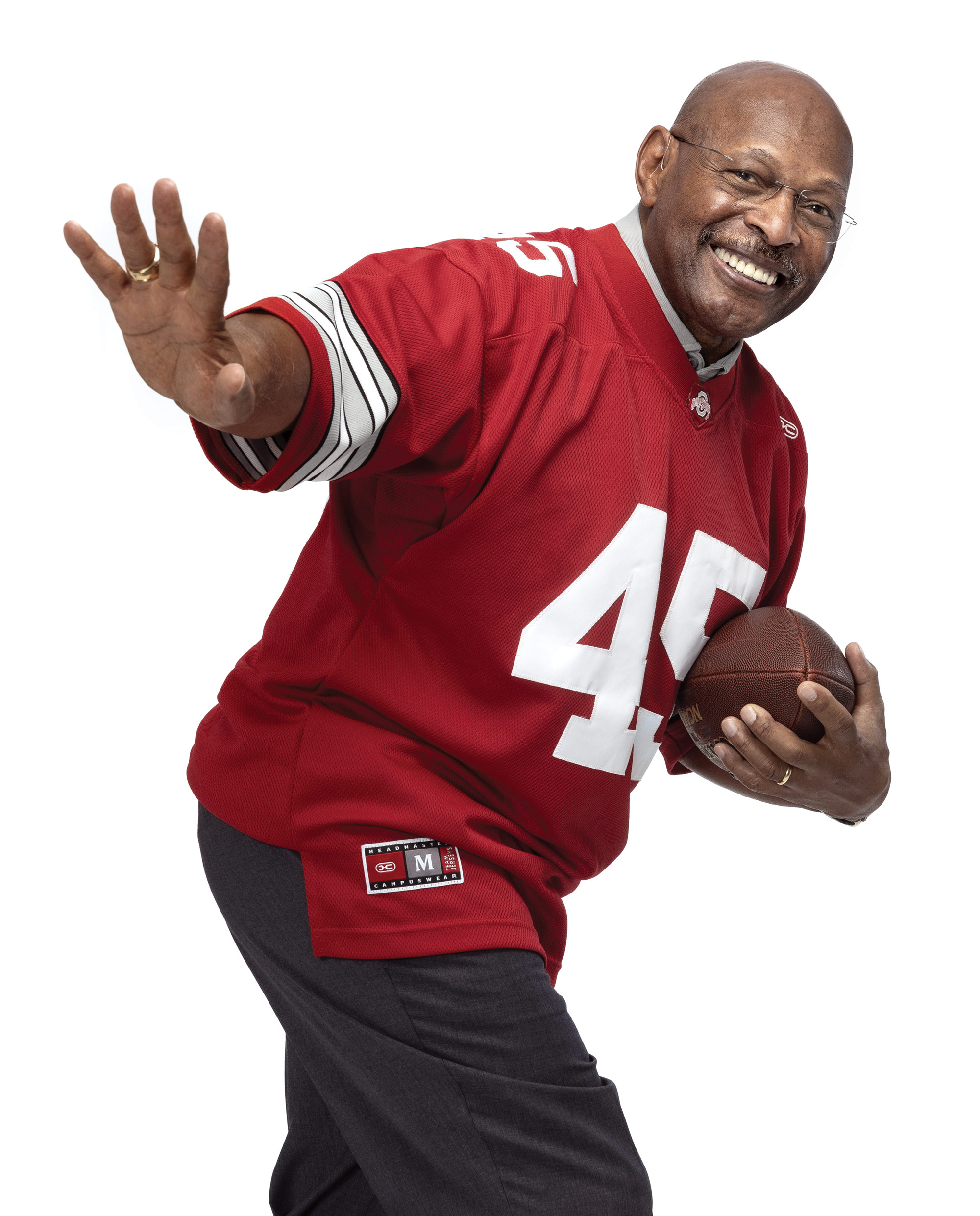 Archie Griffin, a 70-year-old Black man wearing glasses and an Ohio State jersey with his famous number—45, strikes the famous Heisman pose. He carries a football in his left hand and holds out his left as if warding off a defender. Also, his grin says he’s having fun. 