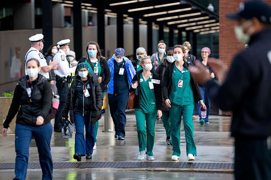 A group of nurses wearing scrubs and face masks walk across the street