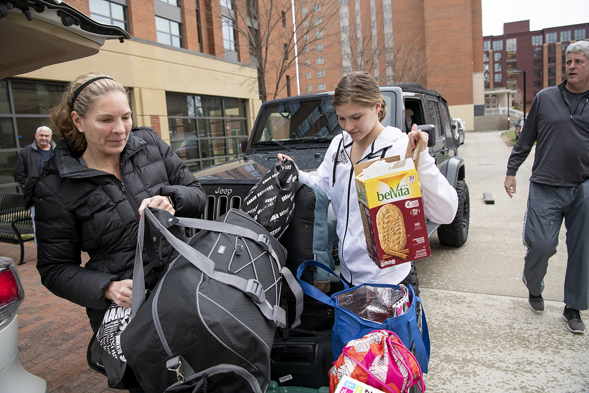 A mother and daughter are lifting duffle bags as they load the student's belongings into a car