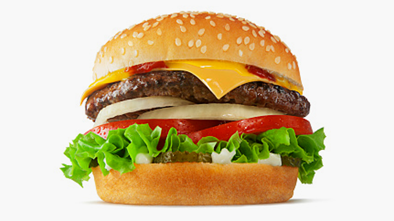 A close-up photo of a large burger containing beef, cheese, onion, tomato and lettuce on a bun with sesame seeds