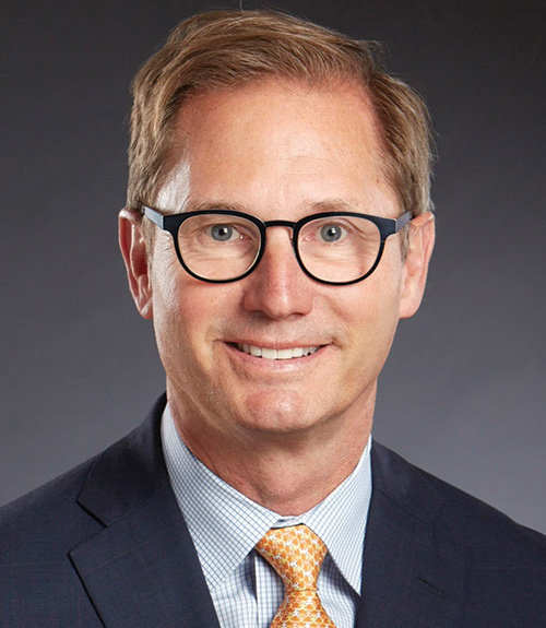 alex fisher portriat wearing a dark suit and tie with glasses on