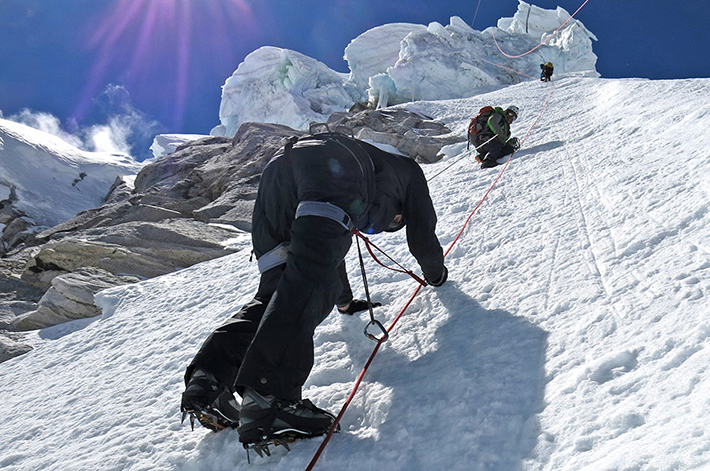 three people in snow gear climbing the side of a mountain